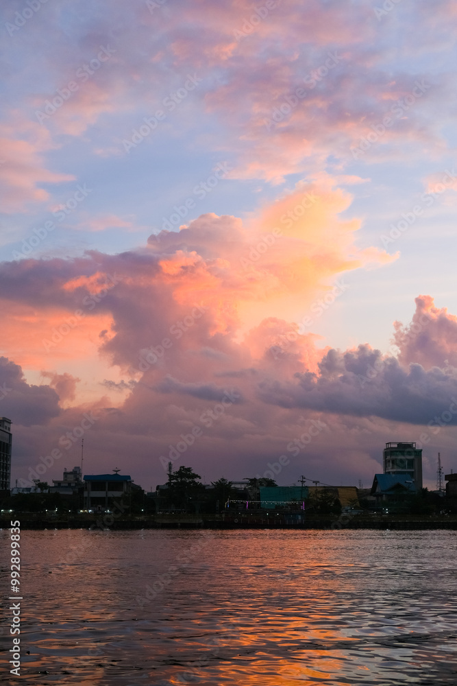 Sunset over Pontianak cityscape at Kapuas River’s edge, with vibrant blue and orange clouds reflecting on the water, capturing the serene beauty of the riverside city.
