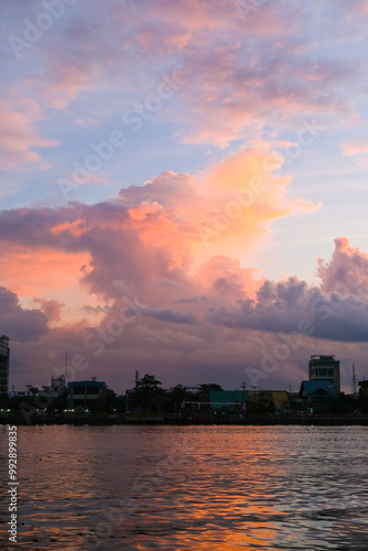 Obraz na płótnie Sunset over Pontianak cityscape at Kapuas River’s edge, with vibrant blue and orange clouds reflecting on the water, capturing the serene beauty of the riverside city. w salonie