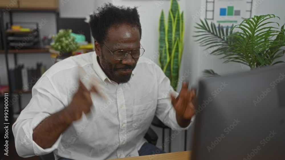 Handsome african american man with a beard working intensely in an indoor office setting, surrounded by plants and office documents. Handsome african american man with a beard working intensely in an indoor office setting, surrounded by plants and office documents.