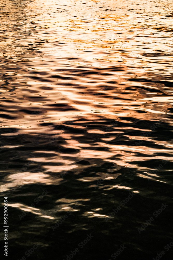 Golden reflections on rippling water create a mesmerizing texture with warm hues and dynamic patterns. Light and shadow interact, forming an abstract, tranquil, and calming natural scene.