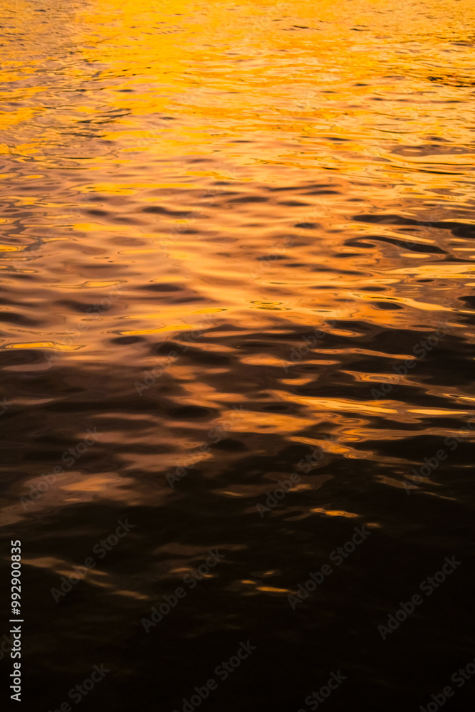 Golden reflections on rippling water create a mesmerizing texture with warm hues and dynamic patterns. Light and shadow interact, forming an abstract, tranquil, and calming natural scene.