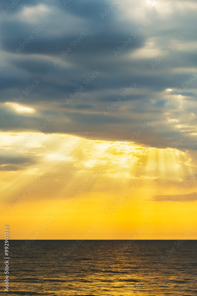 Fototapeta premium Orange sunrise sunrise over sea horizon. Sun rays light drop on colorful clouds on sky. vertical