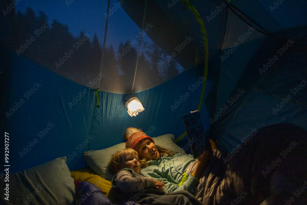 A mother reads to her child in a tent under a light. A mother reads to her child in a tent under a light.