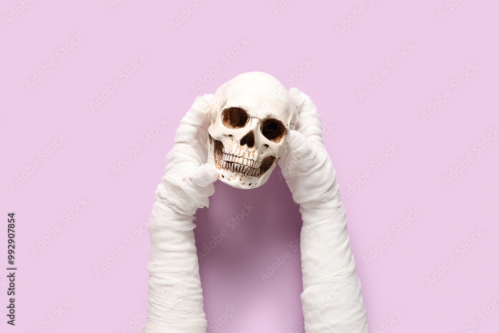 Mummy hands with human skull on purple background. Halloween celebration Mummy hands with human skull on purple background. Halloween celebration