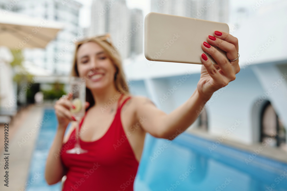 Φωτογραφία Woman wearing red dress standing by swimming pool holding smartphone and cocktai