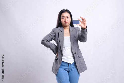 expression of beautiful young office woman pouting holding waist and debit credit card member wearing gray suit standing isolated on white background. for promotional, lifestyle, finance, transaction photo