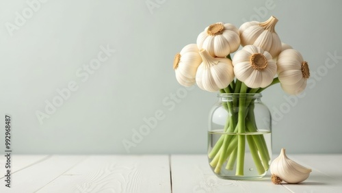 A bouquet of garlic bulbs arranged in a clear glass jar on a light wooden table against a soft green background
Concept: healthy food, natural ingredients, kitchen decor, fresh garlic, organic lifesty photo