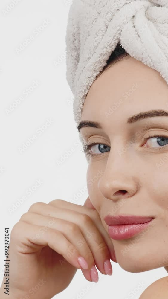 Vertical video. A woman with flawless skin wearing a hair towel after a spa treatment. Her relaxed expression evokes a sense of harmony and self-care against a white background. Vertical video. A woman with flawless skin wearing a hair towel after a spa treatment. Her relaxed expression evokes a sense of harmony and self-care against a white background.