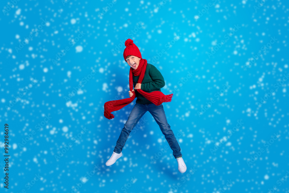 Full length body size photo boy jumping up wearing winter clothes isolated bright blue color background Full length body size photo boy jumping up wearing winter clothes isolated bright blue color background