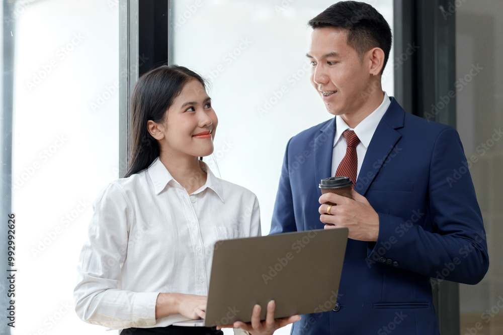 A professional woman and man engage in conversation, smiling, while holding a laptop and a coffee cup in a modern workspace. A professional woman and man engage in conversation, smiling, while holding a laptop and a coffee cup in a modern workspace.