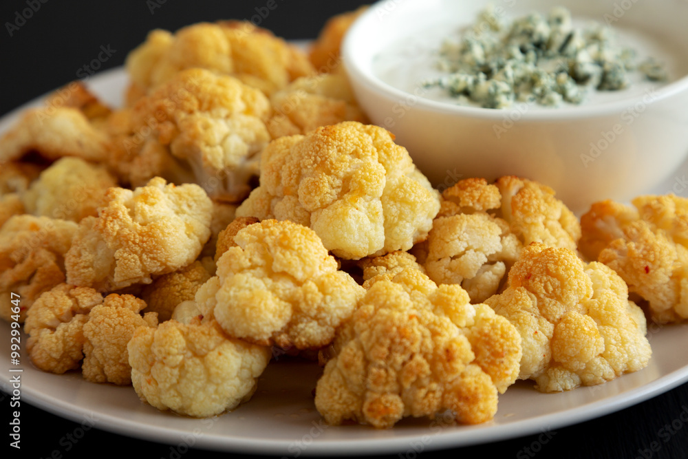 Homemade Buffalo Cauliflower with Blue Cheese Sauce on a Plate on a Black Background, side view. Close-up. Homemade Buffalo Cauliflower with Blue Cheese Sauce on a Plate on a Black Background, side view. Close-up.
