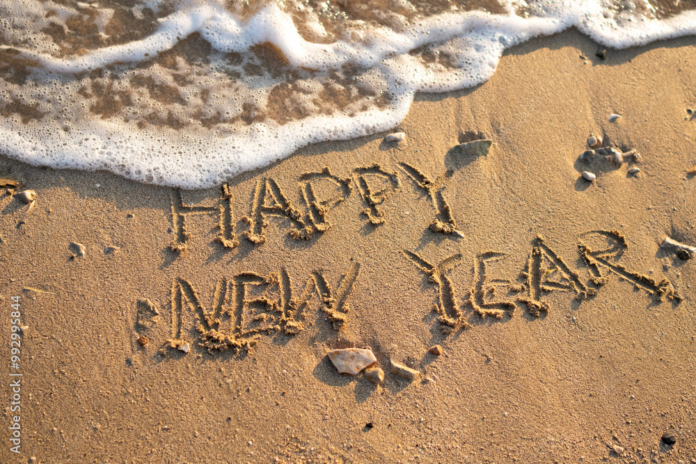 Fototapeta premium Happy new year hand written on a beautiful sand beach. Textured sand with wave. New year concept 