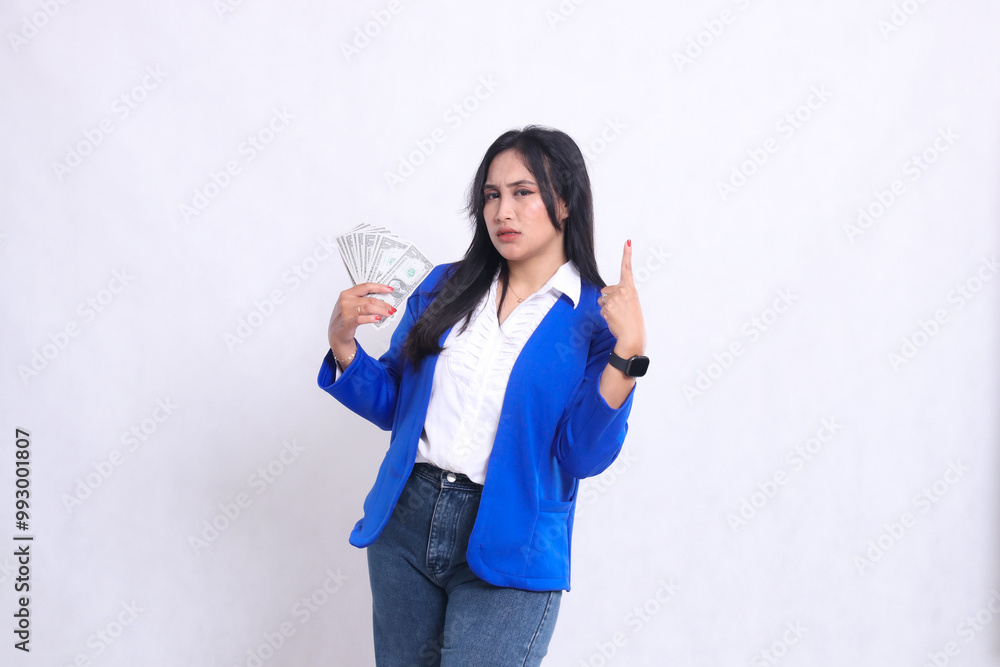 beautiful adult office girl wearing blue formal suit standing angry to camera holding dollar bill to right and pointing up isolated white background. for transaction, finance, business content beautiful adult office girl wearing blue formal suit standing angry to camera holding dollar bill to right and pointing up isolated white background. for transaction, finance, business content