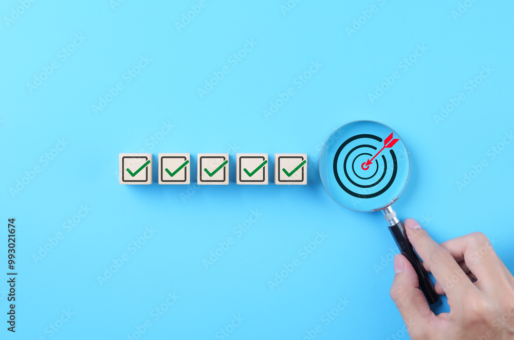 © Supatman - Business Strategy Planning and Quality Management Concept. Magnifying glass focuses on target icon and blocks with check marks. business goal setting, strategy planning, quality management processes,