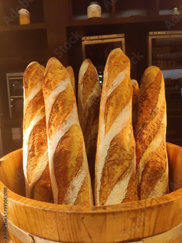 This image showcases a rustic wooden basket filled with freshly baked baguettes. The baguettes, with their golden-brown crusts are beautifully arranged, standing upright in the basket. #bakeryproducts