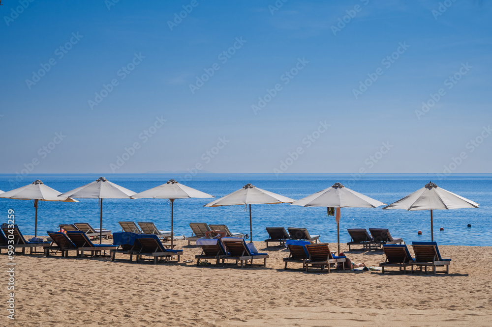 Beach umbrellas with sun beds on sandy beach by sea at the resort during the day in summer Beach umbrellas with sun beds on sandy beach by sea at the resort during the day in summer