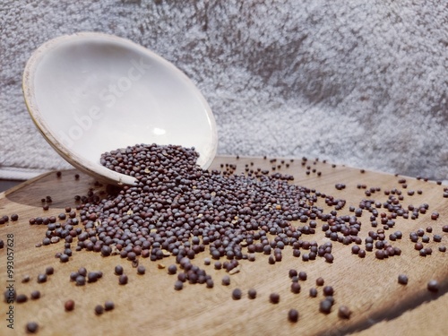 Discover the simplicity and beauty of everyday ingredients with this captivating image of mustard seeds. The photo features a close-up view of tiny, dark mustard seeds spilling from a white bowl.