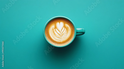 Top view of a latte with latte art in a turquoise mug on a teal background.