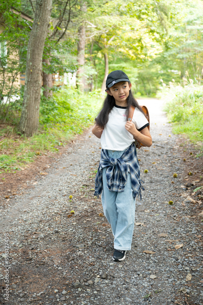 田舎の通学路の森の中を歩く、ランドセルを背負った、下校中の小学生の女の子 田舎の通学路の森の中を歩く、ランドセルを背負った、下校中の小学生の女の子