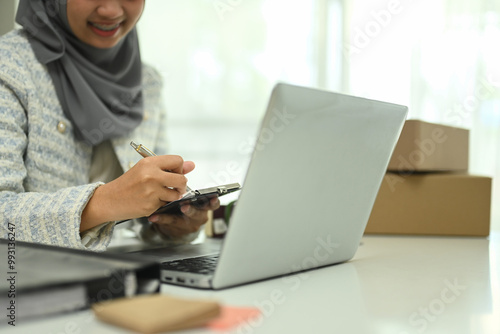 Asian Muslim woman small business owner using laptop for online marketing or checking purchase order