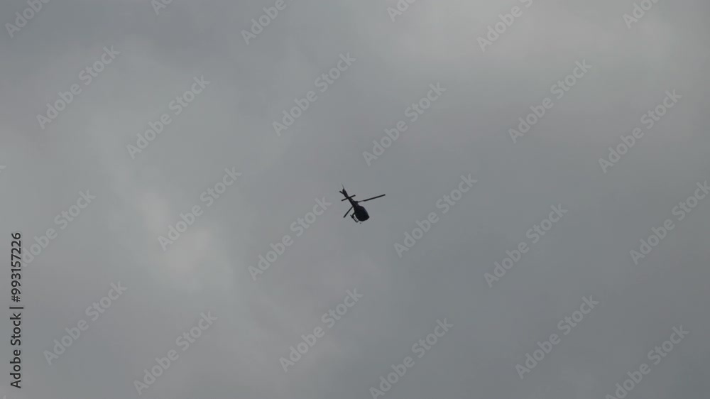 A helicopter flies through the cloudy sky, appearing as a small silhouette against the gray background. A hyperlapse video. A helicopter flies through the cloudy sky, appearing as a small silhouette against the gray background. A hyperlapse video.
