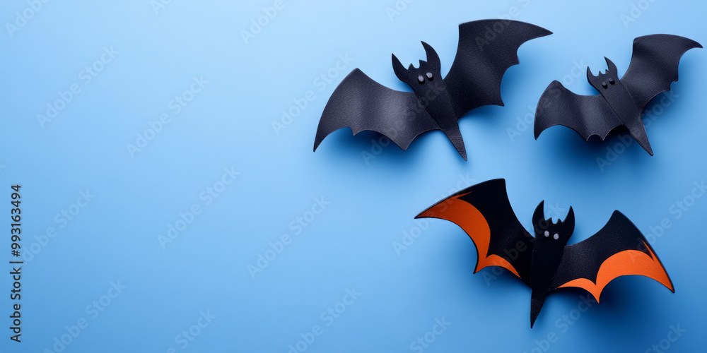 Three decorative bats with black and orange wings are displayed against a light blue background, creating a playful and seasonal atmosphere. Three decorative bats with black and orange wings are displayed against a light blue background, creating a playful and seasonal atmosphere.