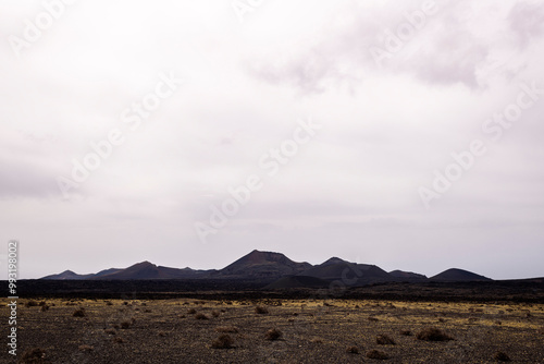 scenery view of volcano Cuervo and rough mountains under cloudy sky in Tinajo, Lanzarote at Canary Islands Spain, concept of dry landscape and adventure travel