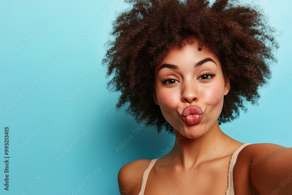 A playful portrait of a woman with an afro hairstyle puckering her lips for a selfie against a bright blue background A playful portrait of a woman with an afro hairstyle puckering her lips for a selfie against a bright blue background