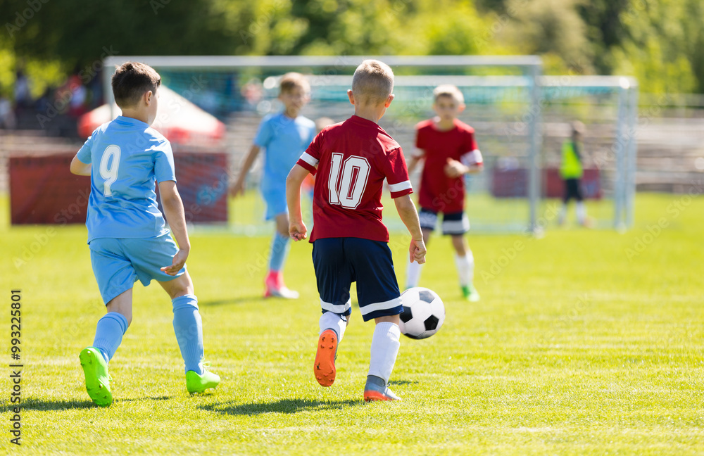 Obraz premium Kids Kicking Football Ball. Boys Play Soccer on Grass Field. Spectators Parents in the Background. Youth Players kicking Soccer Match on grass Stadium. Youth Football Tournament