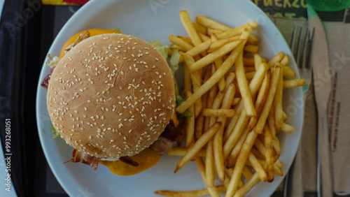 Sabrosa hamburguesa con queso, tocino y huevo sobre un pan de sésamo, acompañada de crujientes papas fritas. Plato de comida rápida listo para servir.