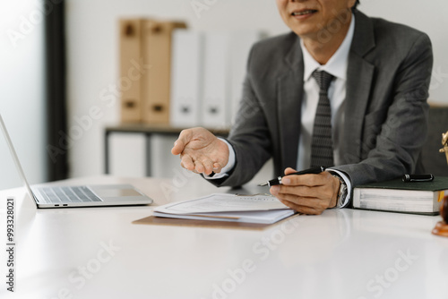 Lawyer Consulting Client:  A serious and professional lawyer in a grey suit sits at his desk, consulting with a client, reviewing important documents.  He gestures towards the papers. photo