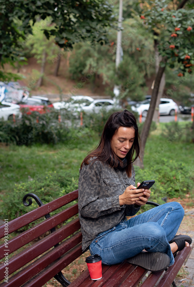 girl using mobile phone in park and drinking coffee. Autumn day girl using mobile phone in park and drinking coffee. Autumn day