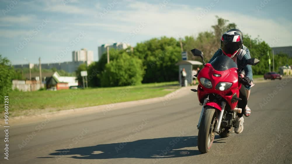 Two sisters, both wearing helmets, ride a red power bike while navigating the road, cars can be seen coming from behind, with a blur of city buildings and electric poles along the roadside Two sisters, both wearing helmets, ride a red power bike while navigating the road, cars can be seen coming from behind, with a blur of city buildings and electric poles along the roadside