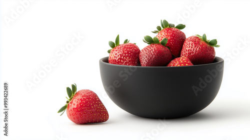 black bowl filled with fresh, ripe strawberries sits on white surface, with one strawberry placed beside bowl. vibrant red color of strawberries contrasts beautifully with black bowl.