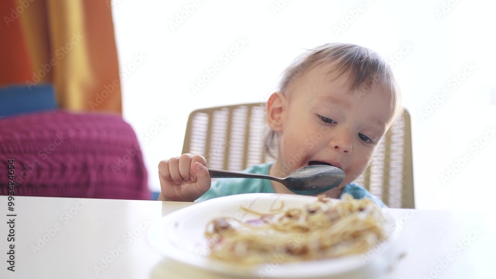 boy eating food at the table. happy family child dream concept. a little boy sits at the table and eats food with a spoon, against the backdrop of a large window. child's food lifestyle boy eating food at the table. happy family child dream concept. a little boy sits at the table and eats food with a spoon, against the backdrop of a large window. child's food lifestyle
