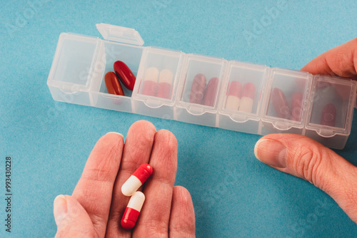 hands holding a plastic organizer pill box for the week white on a blue background
