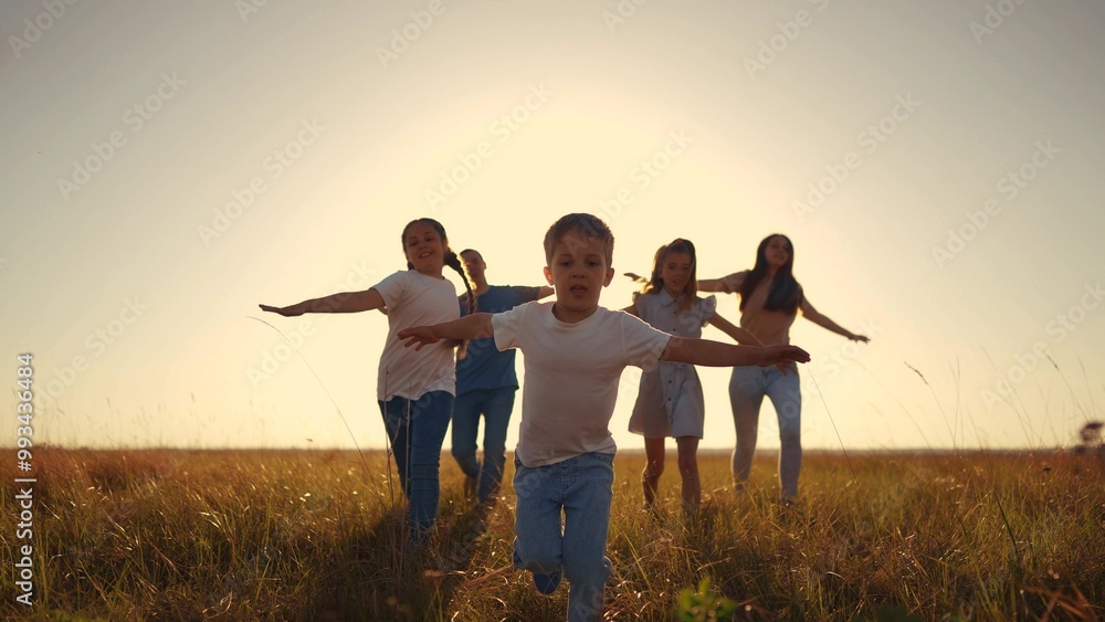 Fototapeta premium children run across the field. people and family concept. a group of happy children running across a large field with their arms outstretched, sunset in the background lifestyle