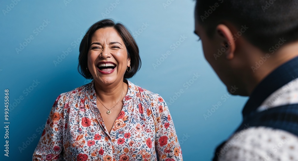 Laughing middleaged Hispanic woman with short hair wearing floral blouse on plain blue background Laughing middleaged Hispanic woman with short hair wearing floral blouse on plain blue background