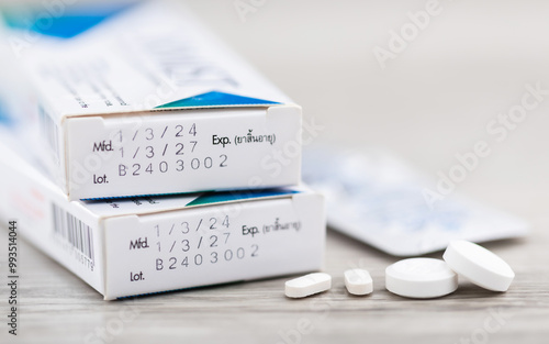 Close-up of the production code and expiration date printed on the side of a medicine box, with pills placed on a table. The image highlights the importance of checking medication before consumption photo