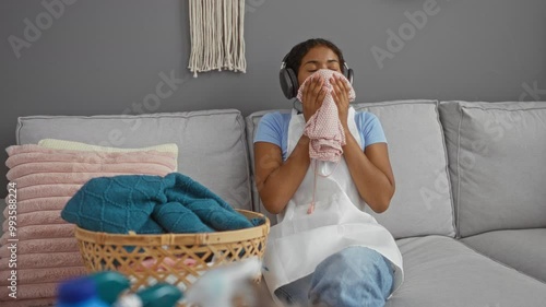 Woman smelling clean laundry wearing headphones in living room with woven basket and cozy cushions photo