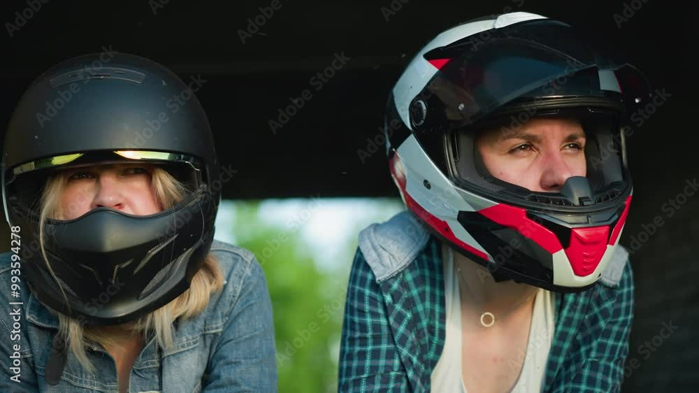 Two women in helmets leaning forward, intensely focused on something off-screen, one is in a black helmet and the other in a red and white helmet Two women in helmets leaning forward, intensely focused on something off-screen, one is in a black helmet and the other in a red and white helmet
