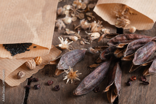 Seeds of garden flowers in small paper bags and glasses on wooden table