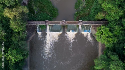 Aerial photograph shot of a dam with water flowing through it, surrounded by dense green foliage and a tranquil natural environment.