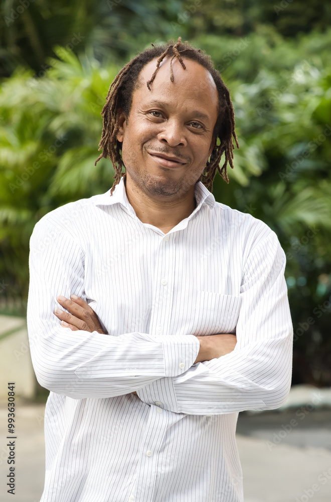 Cool, happy, smiling relaxed middle aged African man crossing arm in green outdoor park summer Cool, happy, smiling relaxed middle aged African man crossing arm in green outdoor park summer