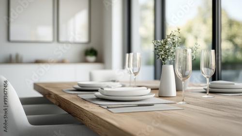 A beautifully arranged dining table, set with white plates, glasses, and a centerpiece vase with greenery, illuminated by natural light from large windows in a contemporary room.