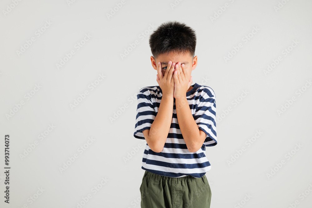 Asian portrait young kid boy in depressed bad mood covering face with hands and peering out with one eye between fingers studio shot isolated on white background, primary child surprised and shocked Asian portrait young kid boy in depressed bad mood covering face with hands and peering out with one eye between fingers studio shot isolated on white background, primary child surprised and shocked