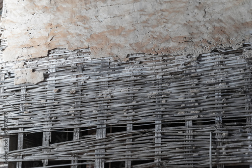A weathered brick wall with peeling plaster and exposed red bricks. A row of woven bamboo sticks forms the top of the wall.