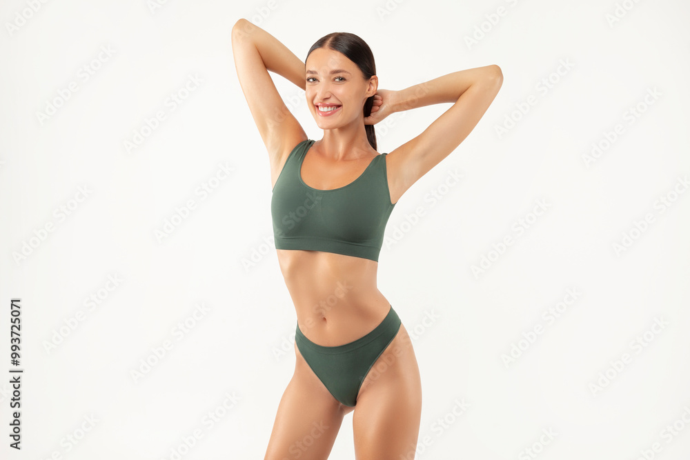 Happy European woman in green lingerie posing with hands behind head and smiling at camera over white studio background, showing smooth armpits and slender body shape Happy European woman in green lingerie posing with hands behind head and smiling at camera over white studio background, showing smooth armpits and slender body shape
