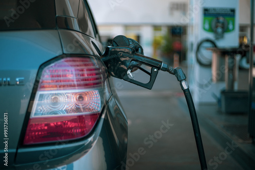 Automóvil gris siendo abastecido de combustible en una estación de servicio. Primer plano de la boquilla de la bomba de gasolina