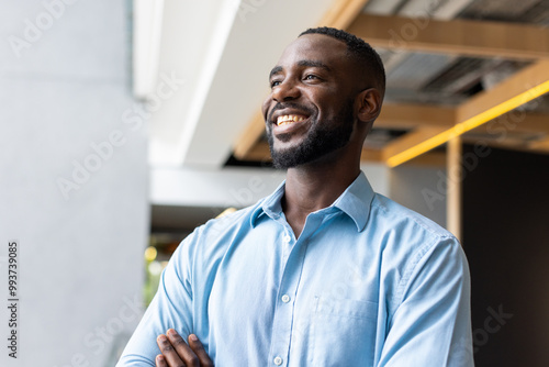 Canvas Print Smiling african american man in blue shirt standing confidently in modern office